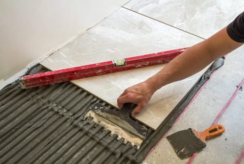 Ceramic tiles and tools for tiler. Worker hand installing floor tiles. Home improvement, renovation – ceramic tile floor adhesive, mortar, level. Ceramic tiles and tools for tiler. Worker hand installing floor tiles. Home improvement, renovation - ceramic tile floor adhesive, mortar, level